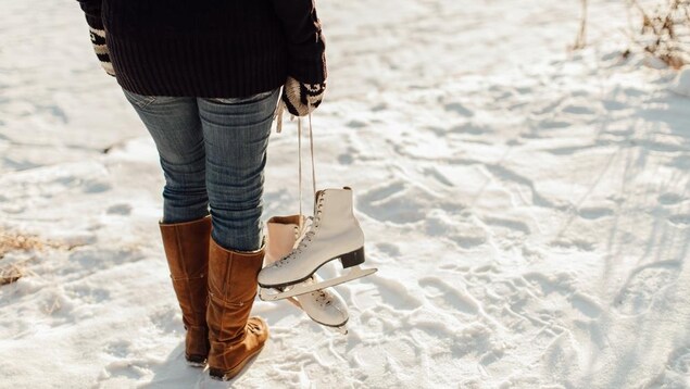 Une femme en bottes d'hiver tient une paire de patins.