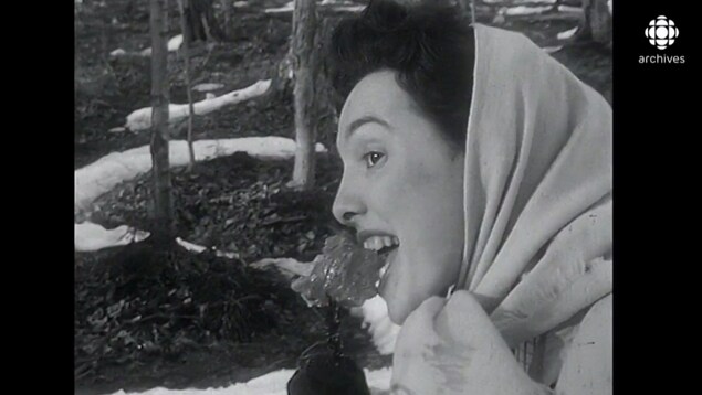 Femme, de profil, qui mange un gros morceau de tire d'érable sur un bâton. 