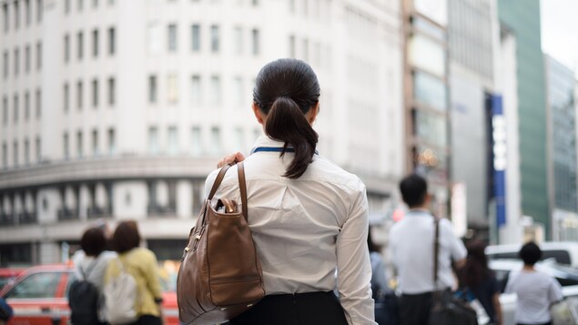 Une femme de dos se tient en face d'une rue achalandée d'un centre-ville.