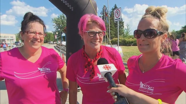 Trois femmes vêtues de rose sourient et répondent à la journaliste. Trois femmes vêtues de rose sourient et répondent à la journaliste.