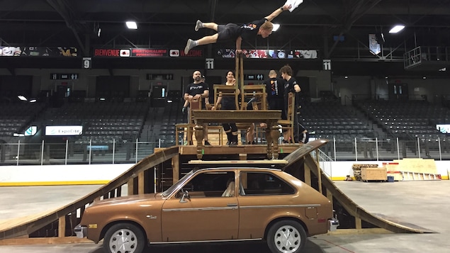 Une troupe de cirque fait une prouesse avec un artisan qui se tient à une main sur deux chaises