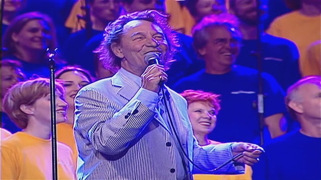Jean-Pierre Ferland chante avec des choristes derrière lui.