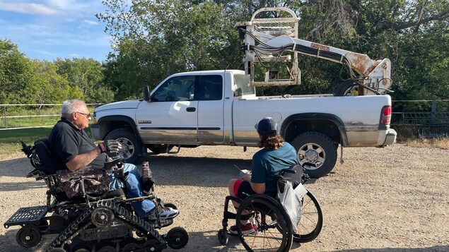 Deux hommes en fauteuil roulant devant une camionnette.