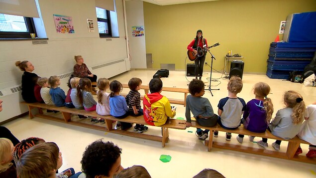 Des jeunes du primaire regardent une prestation musicale dans un gymnase.