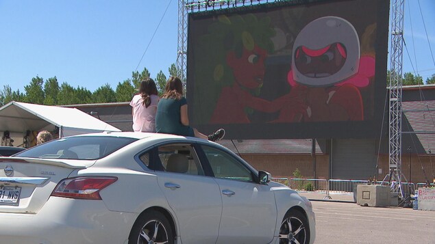 Deux jeunes filles sur le toit d'une voiture regardent un film sur grand écran.