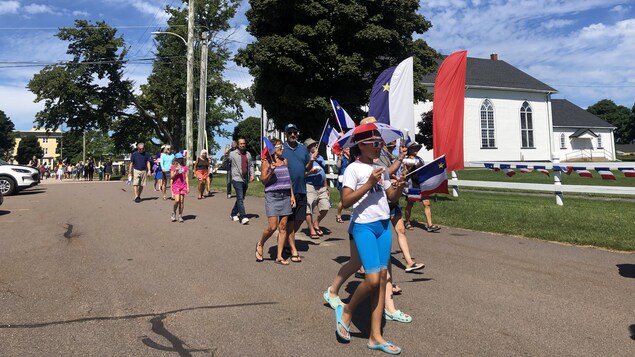 Des personnes habillées aux couleurs de l’Acadie marchent dans une rue lors d’un tintamarre. 