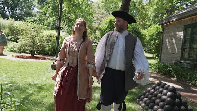 Un homme et une femme en costumes du XVIe siècle circulent sur un site historique, l'été
