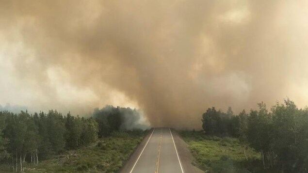 L'épaisse fumée d'un feu de forêt au bout d'une autoroute déserte.