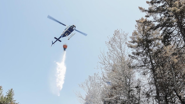 De l'eau tombe d'un hélicoptère qui survole un feu de forêt.
