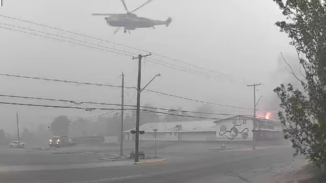 Un hélicoptère arrose un bâtiment en feu dans la ville de La Ronge obscurcie par la fumée.
