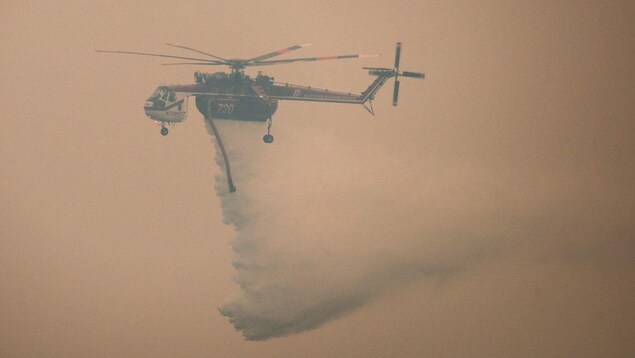 Un hélicoptère dans les airs. Il est difficile de le voir en raison de l'épaisse fumée dans le ciel.
