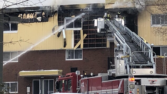 Des pompiers au sommet de l'échelle combattent l'incendie au deuxième étage du bâtiment.
