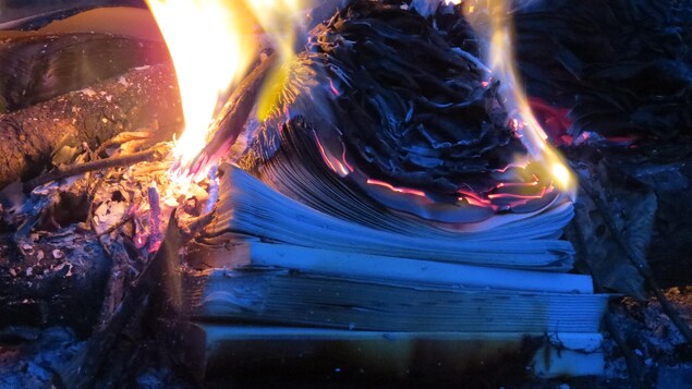 Un livre brûle dans un foyer extérieur.
