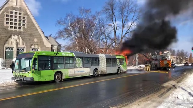 L'arrière d'un bus en flammes et des pompiers qui les combattent