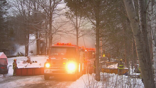 Des camions de pompiers sont devant une maison en fumée.