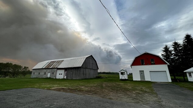 Une grange et un garage devant de l'épaisse fumée qui monte dans le ciel.