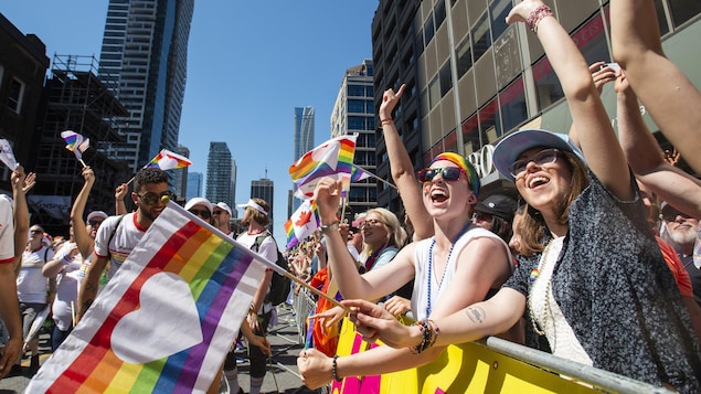 Des femmes brandissent un drapeau arc-en-ciel et sourient.