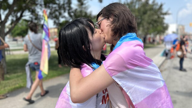 Un couple s'embrasse sur le boulevard Memorial à Winnipeg, enveloppé d'un drapeau transgenre, le 4 juin 2023. 