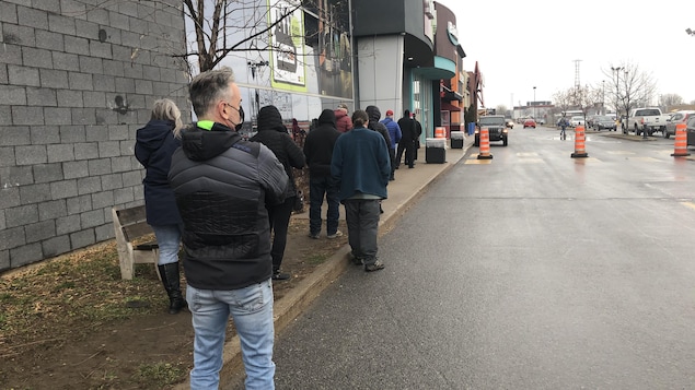 Une file de gens à l'extérieur d'un commerce.