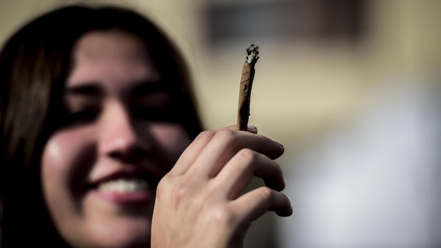 Une jeune fille souriante tient un joint dans sa main.