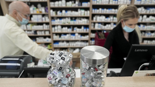 Deux employés s'affairent derrière des contenants remplis de fioles de vaccin vides dans une pharmacie torontoise.
