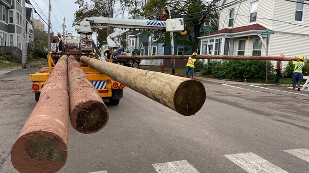 Des ouvriers remplacent un poteau le long d'une rue. Leur équipement bloque la rue.