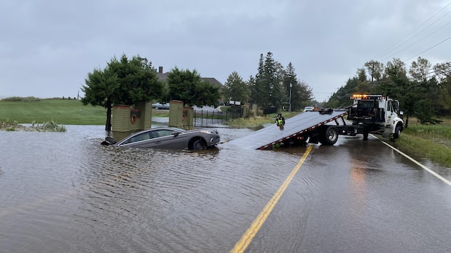 Un véhicul  submergé par les eaux sur une route. Un camion tente de récupérer la voiture.