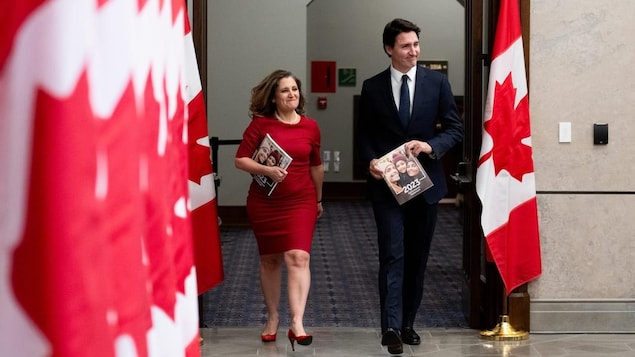 Chrystia Freeland and Justin Trudeau, all smiles, walk by a row of Canadian flags.