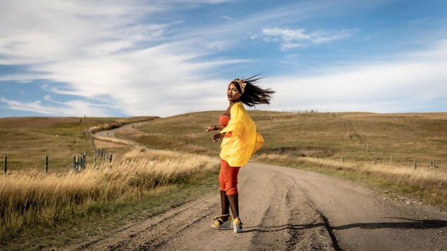 La danseuse Flany Ba danse dans une vallée devant une route sinueuse.