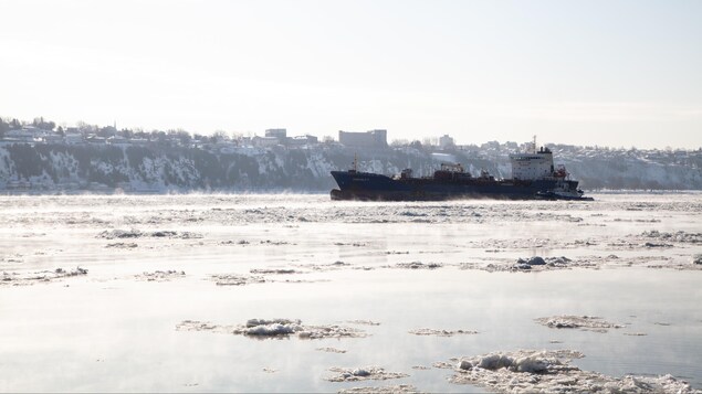 Un bateau de transport est sur le fleuve plein de glace et de vapeur, causées par le froid.