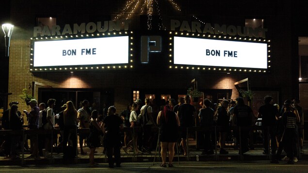 People wait in front of a Rouyn-Noranda hall that displays “Good FME.”