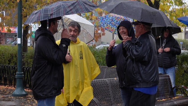 Des hommes discutent dans la bonne humeur, sous des parapluies.