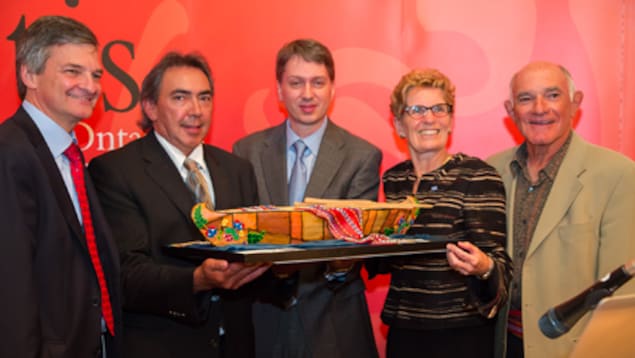 Des politiciens et représentants métis tiennent une maquette d'un bateau en bois. Des politiciens et représentants métis tiennent une maquette d'un bateau en bois.