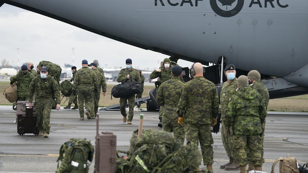 Des militaires sur le tarmac d'un aéroport portent des équipements.