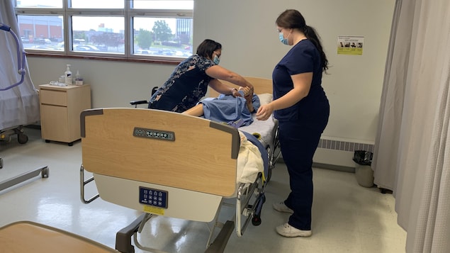 Deux femmes pratiquent des manœuvres sur un mannequin dans un lit d'hôpital.
