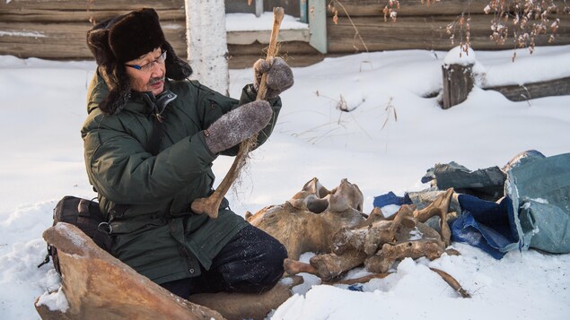 Un historien sibérien examine les restes d'un mammouth, à genoux dans la neige.