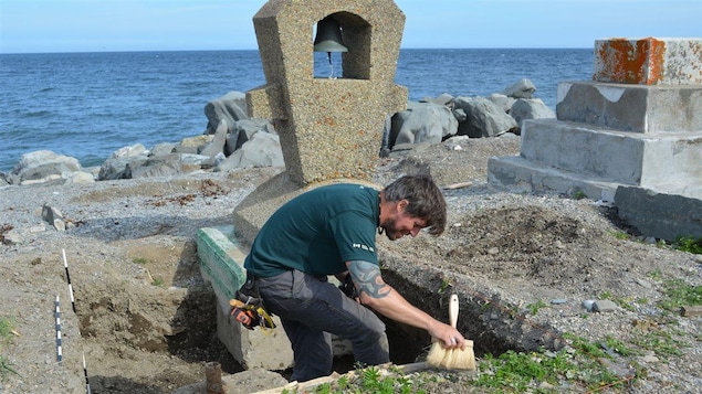 Un homme balaie de la terre à l'aide d'un petit balai près de la cloche du monument.