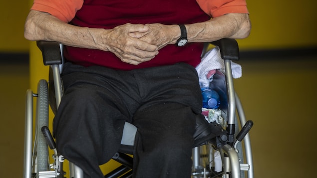 Un octogénaire qui n'a qu'une jambe est assis tranquillement dans un fauteuil roulant, les deux mains croisées sur le ventre.