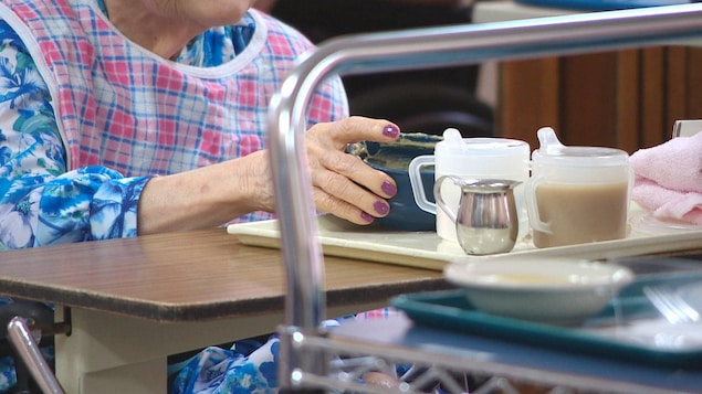 Gros plan sur la main d'une dame âgée qui tient un bol de nourriture.
