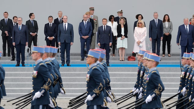 Emmanuel macron et des membres du gouvernement regardent défiler des militaires.