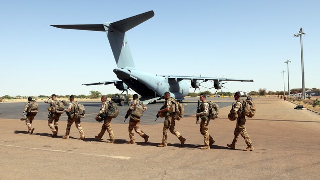 Des militaires français marche sur la tarmac d'un aéroport où se trouve un avion.