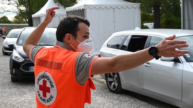 Un homme en dossard orange dirige des voitures.