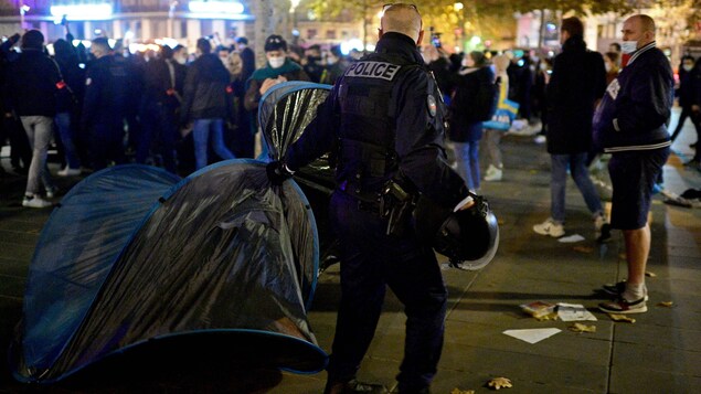 Un gendarme français tire sur une tente, près d'une foule.
