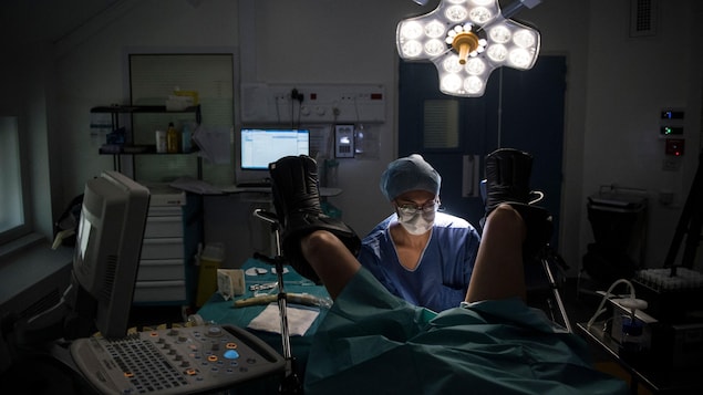 Une gynécologue opère une personne dans une salle opératoire. 