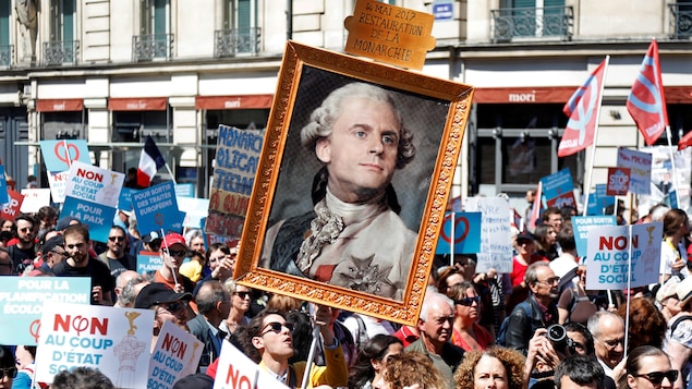 Des manifestants brandissant un cadre où l'on peut voir Emmanuel Macron en royauté française. Des manifestants brandissant un cadre où l'on peut voir Emmanuel Macron en royauté française.