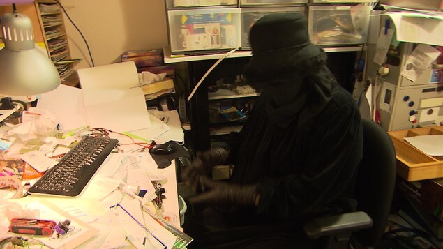 Une femme couverte de noir est assise devant une table d'ordinateur ensevelie sous une montagne de papiers.
