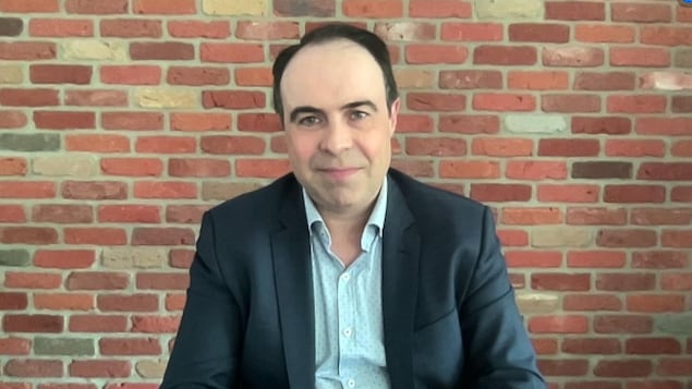 Un homme en visioconférence devant un mur de briques.