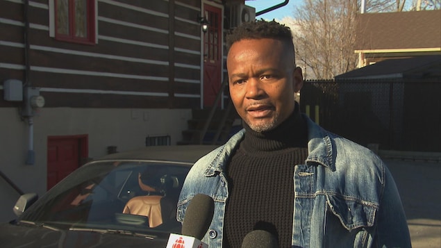 François Ducas donne une entrevue à la caméra devant sa voiture de marque BMW.