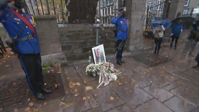 Une photo et des fleurs ont été déposées au sol, et sont entourées de deux policiers.
