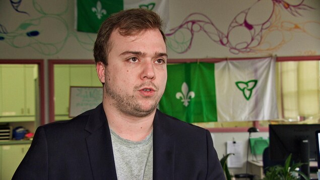 Un jeune homme en entrevue devant des drapeaux franco-ontariens.